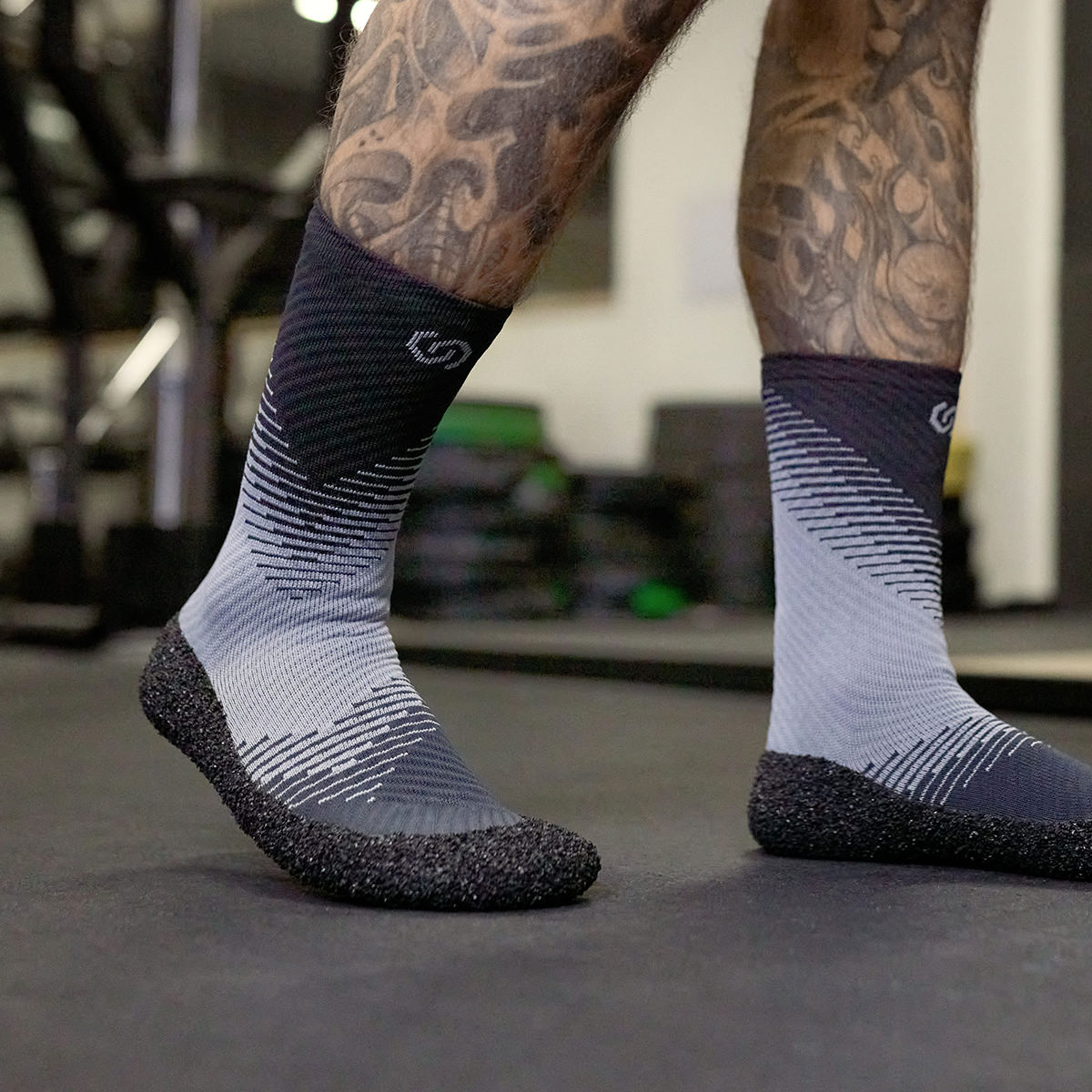 Close up of a person's feet wearing Skinners compression socks walking across a gym floor.